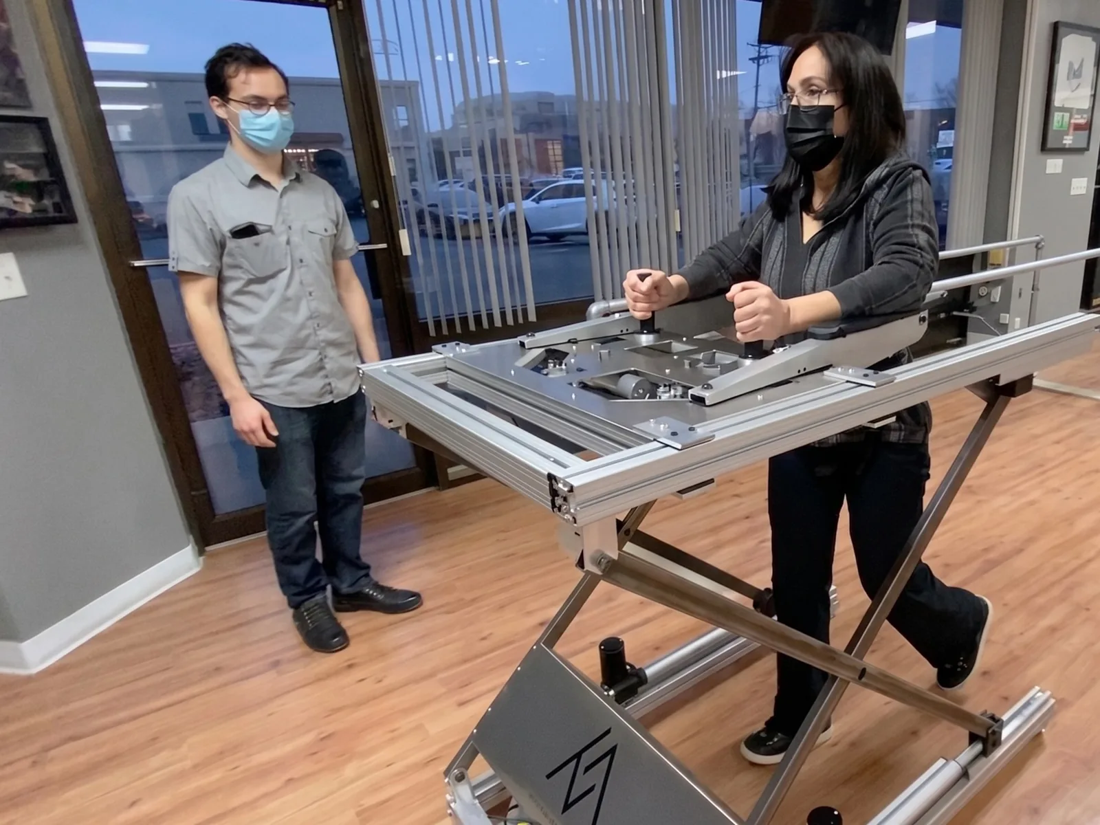 A patient walks in an early-stage Enlighten Mobility gait-trainer prototype, supported by a member of the team.