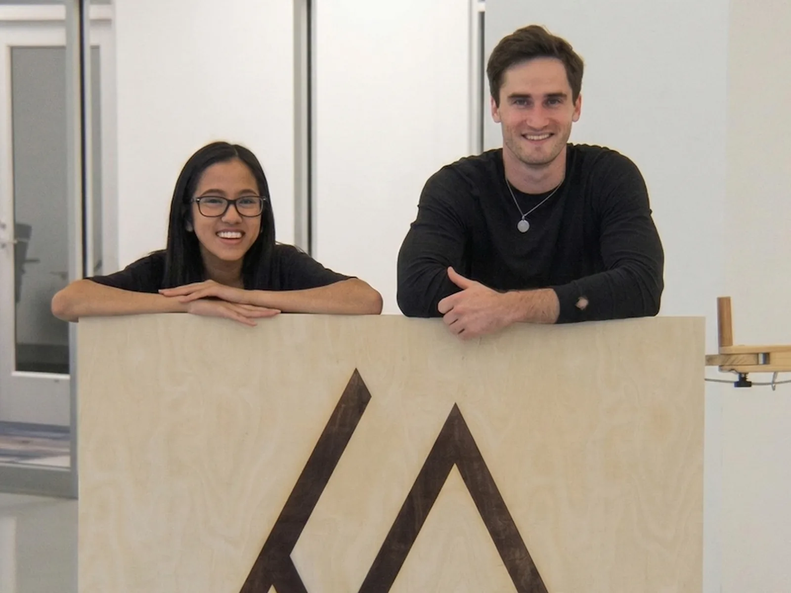 Leanne and Jeff of the Enlighten Mobility team, smiling behind a hand-built wooden Enlighten Mobility brand board.
